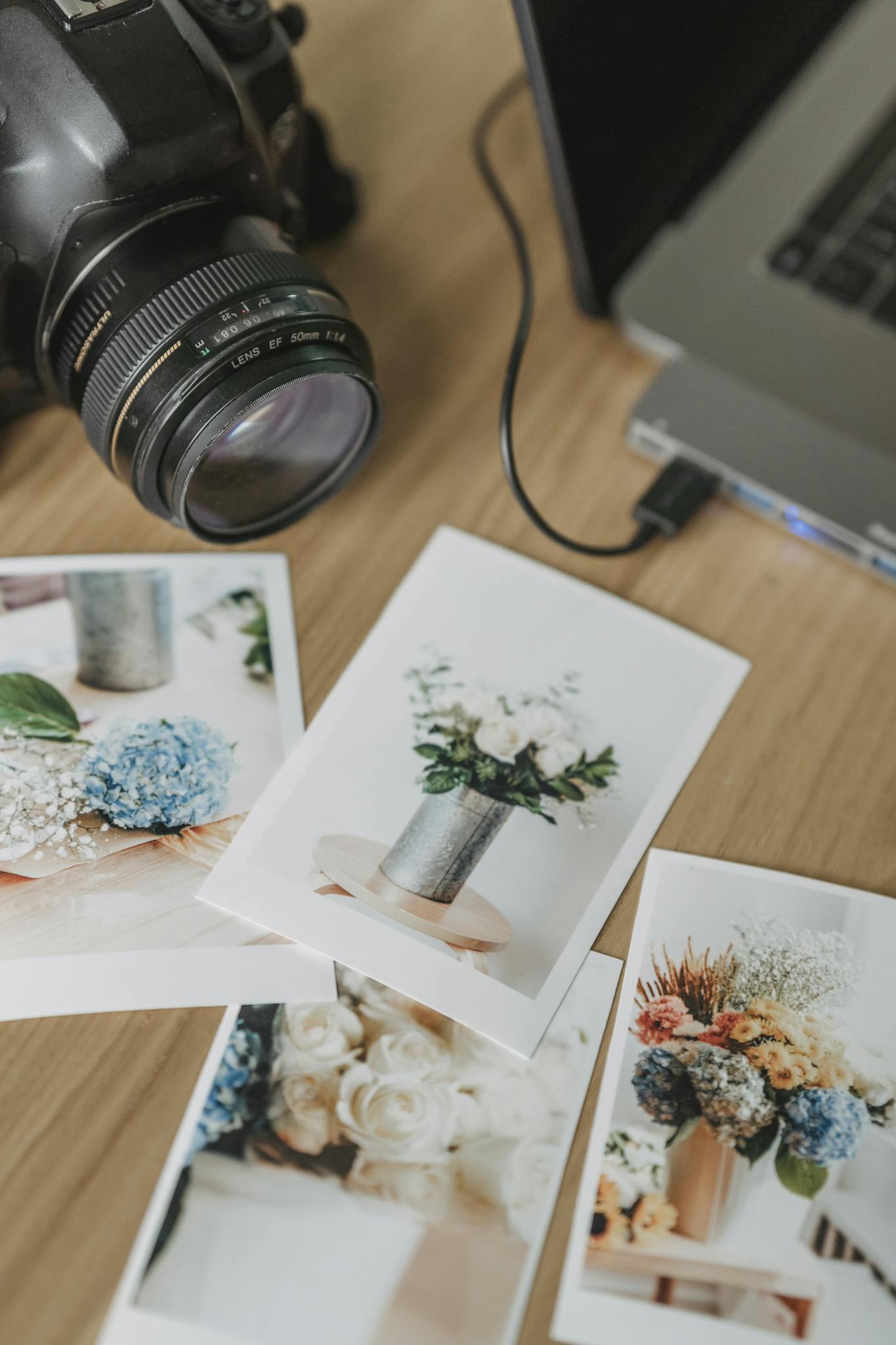 Camera and laptop on a desk with printed floral images, showing photography setup.