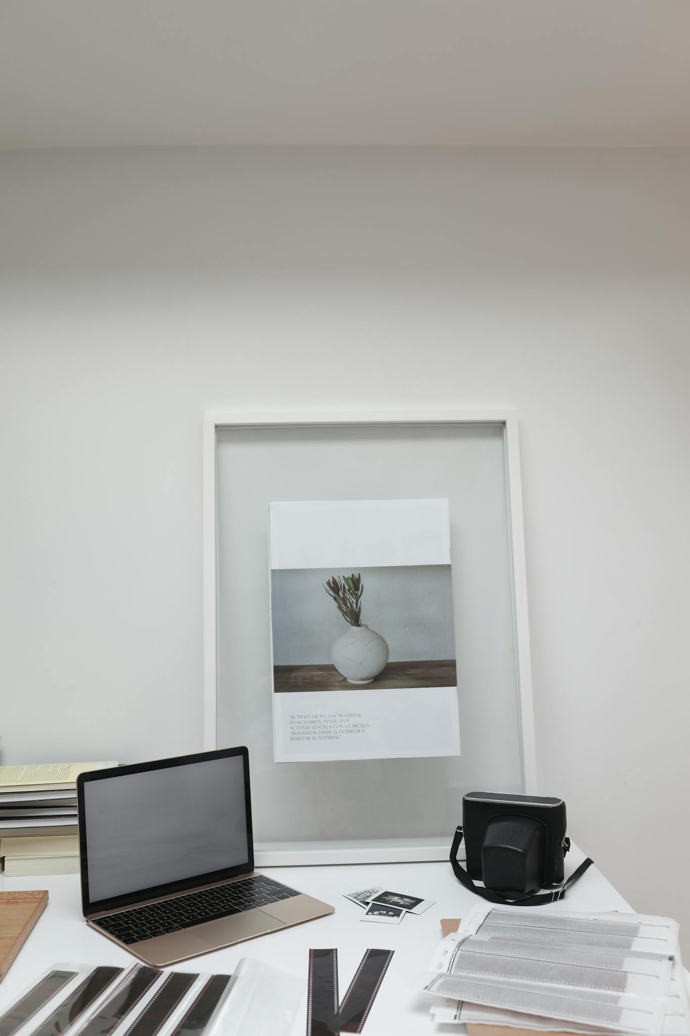 Minimalist workspace featuring a laptop, camera, and framed art on a desk.